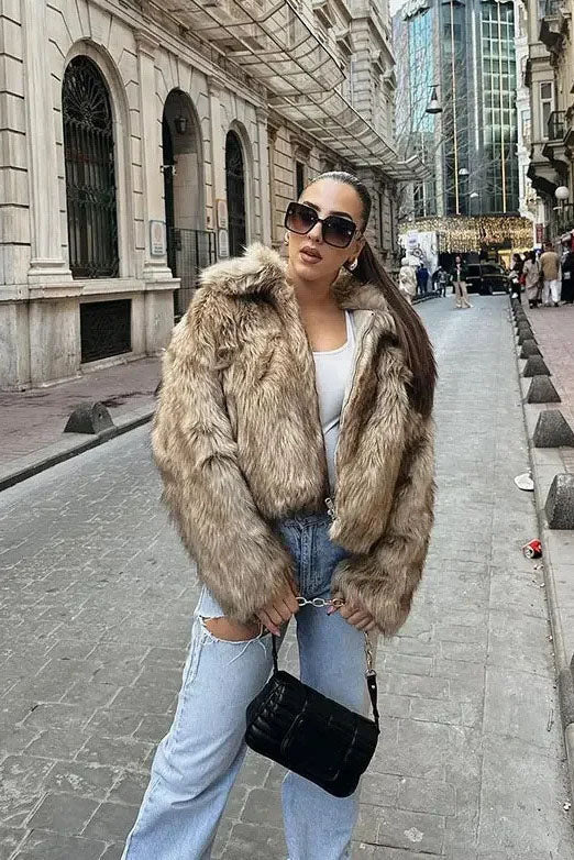 Brown - A woman sits on the hood of a vintage car wearing a fluffy, light brown faux fur cropped jacket with a large collar, styled with light wash wide-leg jeans.