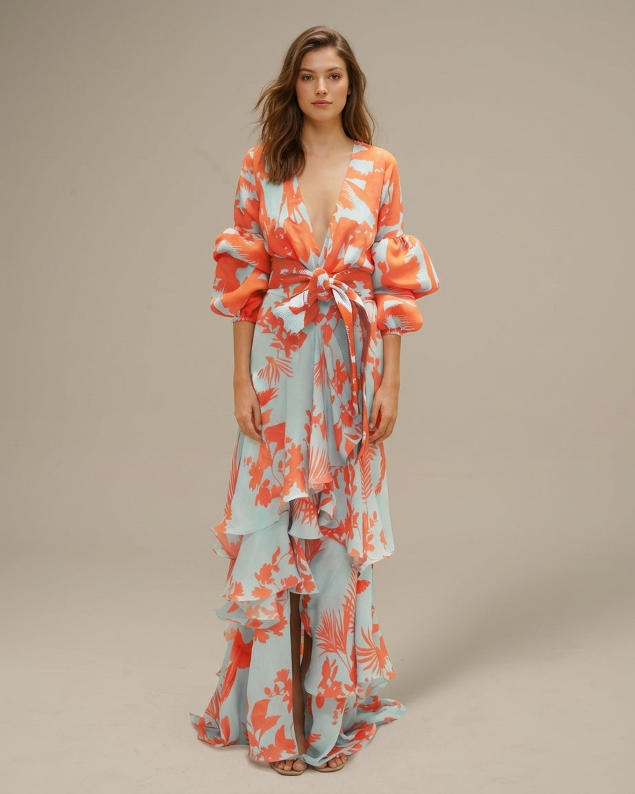Orange - A woman wearing a pale blue and mustard yellow botanical print maxi dress featuring a deep V-neckline, voluminous balloon sleeves, a belted waist, and a cascading tiered ruffle skirt.