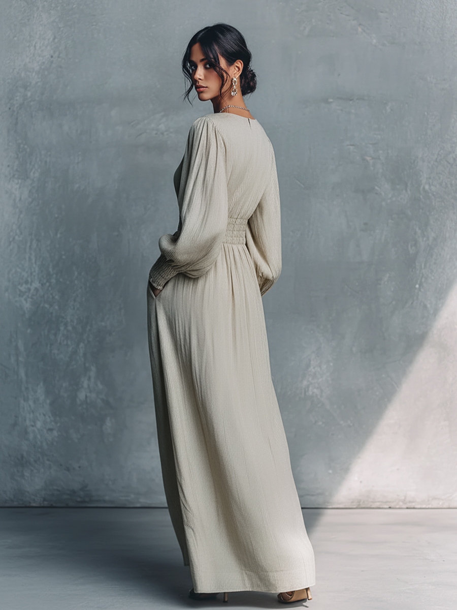 Beige - A woman wearing a champagne-coloured, crinkle-textured crepe maxi dress featuring a plunging V-neckline, long balloon sleeves with shirred cuffs, a smocked waistband with a drawstring, and a flowing floor-length skirt.