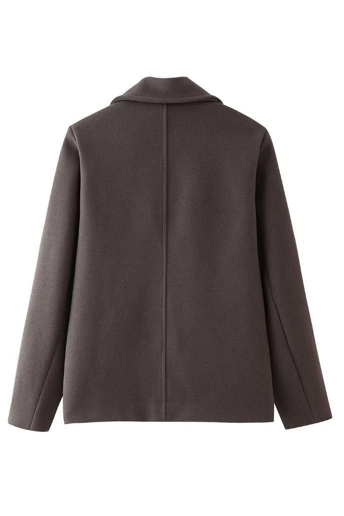 Grey - A woman walking outdoors wearing a taupe-coloured, textured double-breasted short pea coat with wide notched lapels and an oversized fit, styled over a black top and high boots.