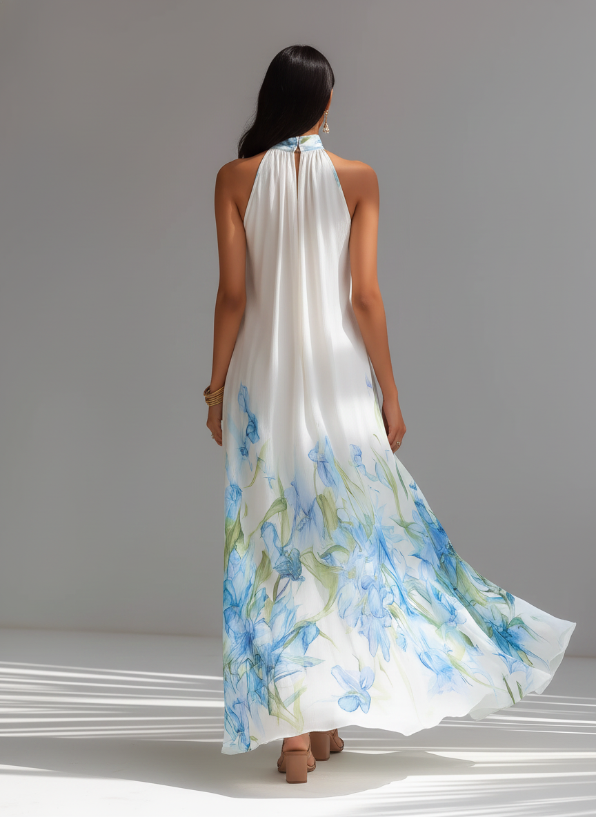 White Printed - A model wears a sleeveless, high halter neck maxi dress made of flowing white chiffon with a blue and green watercolour floral print cascading down the voluminous skirt.