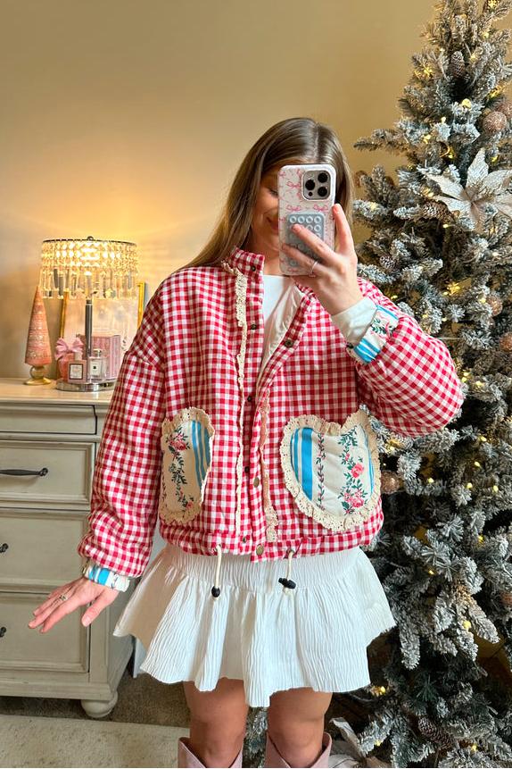 Women's cropped quilted jacket featuring a red and white gingham pattern, button-front closure, lace trim, and contrast floral heart-shaped patch pockets, worn over a white mini skirt.