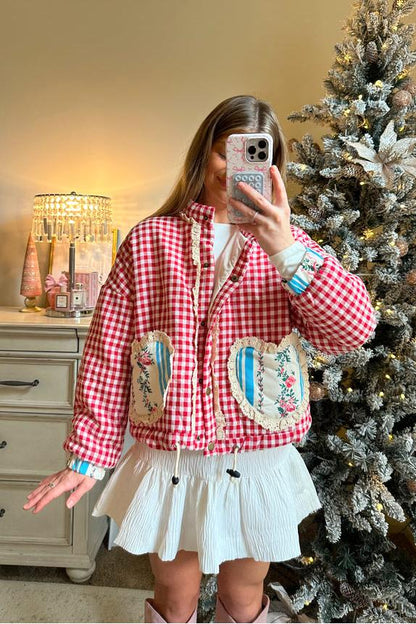 Women's cropped quilted jacket featuring a red and white gingham pattern, button-front closure, lace trim, and contrast floral heart-shaped patch pockets, worn over a white mini skirt.