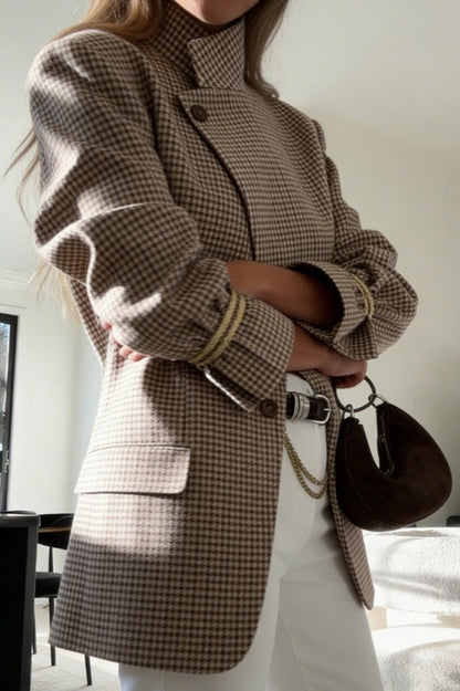 Plaid - A woman wearing a relaxed-fit, mid-length houndstooth jacket featuring an asymmetric high collar and distinctive ruched sleeves with tie details.
