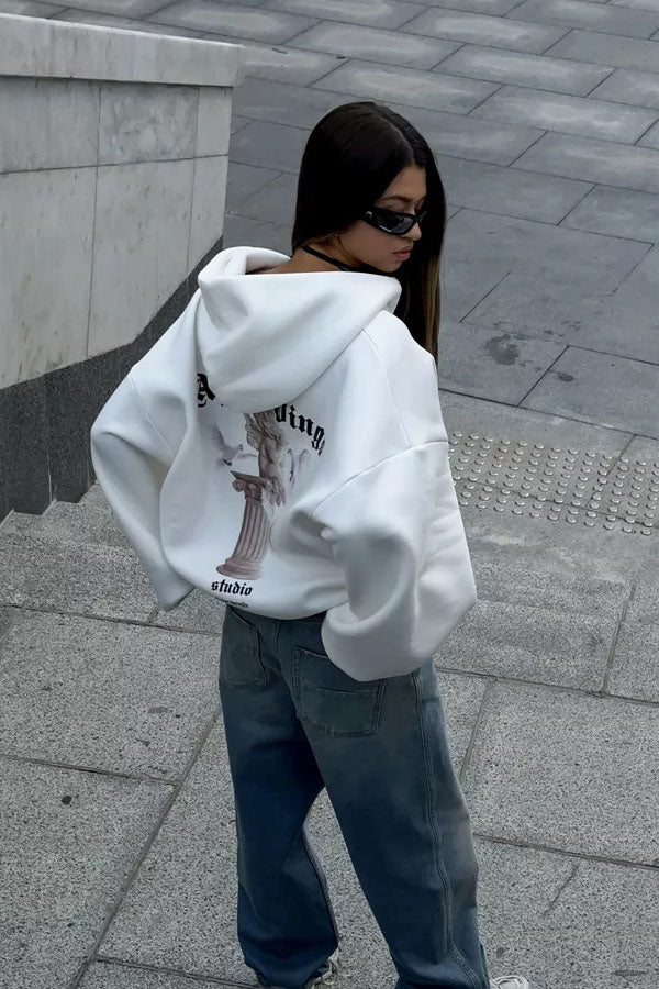 White - Back view of a woman wearing a dark grey oversized hoodie featuring a large graphic print of an angel statue and white doves, paired with a dark grey pleated mini skirt.