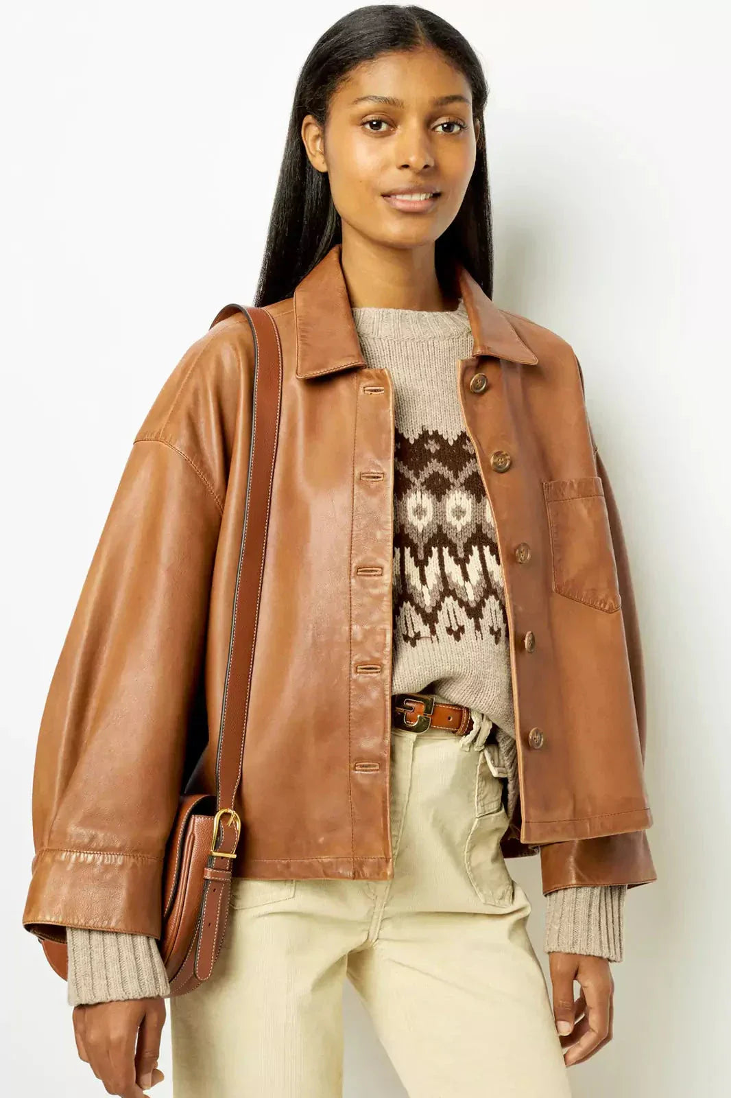 Brown - A woman wearing a relaxed-fit, brown faux leather button-front jacket with a classic collar and single chest pocket, styled over a patterned knit sweater.
