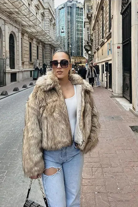 Brown - A woman sits on the hood of a vintage car wearing a fluffy, light brown faux fur cropped jacket with a large collar, styled with light wash wide-leg jeans.
