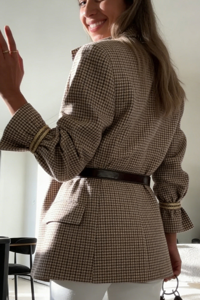 Plaid - A woman wearing a relaxed-fit, mid-length houndstooth jacket featuring an asymmetric high collar and distinctive ruched sleeves with tie details.