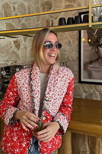 A woman wearing a hip-length quilted jacket featuring a mixed red and white floral print, contrast dark piping, and a button-front closure.