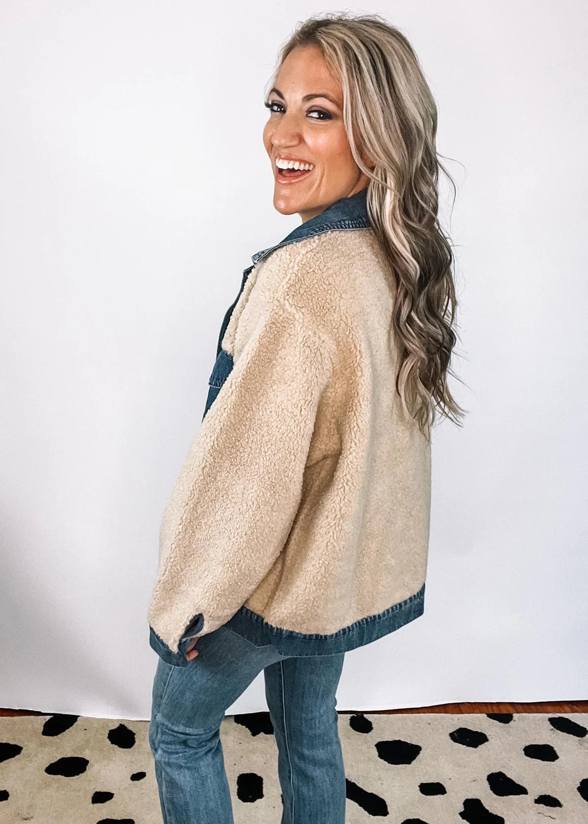XL - A woman smiling wearing a heavyweight mixed-media jacket featuring a blue denim collar, placket, and chest pockets contrasted with a plush, beige sherpa body and sleeves.