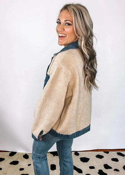 XL - A woman smiling wearing a heavyweight mixed-media jacket featuring a blue denim collar, placket, and chest pockets contrasted with a plush, beige sherpa body and sleeves.