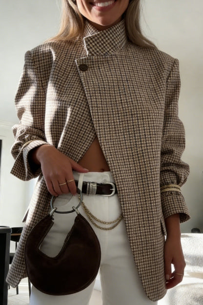 Plaid - A woman wearing a relaxed-fit, mid-length houndstooth jacket featuring an asymmetric high collar and distinctive ruched sleeves with tie details.
