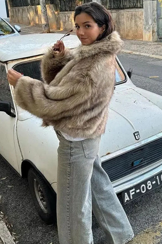 Brown - A woman sits on the hood of a vintage car wearing a fluffy, light brown faux fur cropped jacket with a large collar, styled with light wash wide-leg jeans.