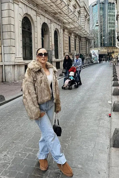 Brown - A woman sits on the hood of a vintage car wearing a fluffy, light brown faux fur cropped jacket with a large collar, styled with light wash wide-leg jeans.