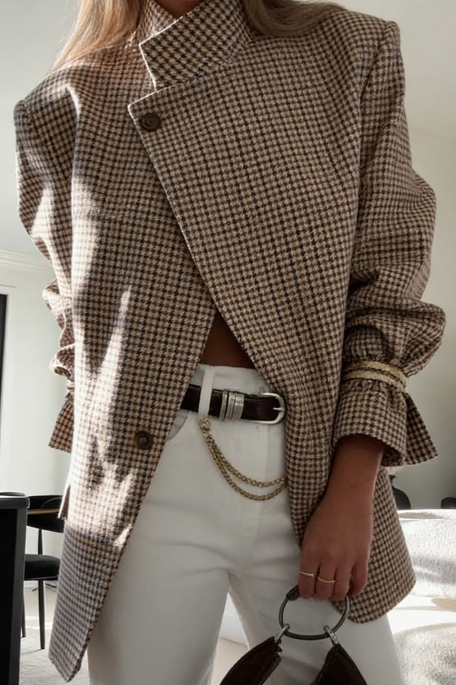 Plaid - A woman wearing a relaxed-fit, mid-length houndstooth jacket featuring an asymmetric high collar and distinctive ruched sleeves with tie details.