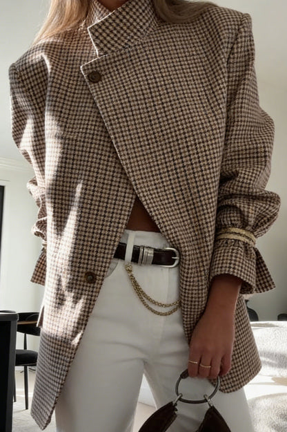 Plaid - A woman wearing a relaxed-fit, mid-length houndstooth jacket featuring an asymmetric high collar and distinctive ruched sleeves with tie details.