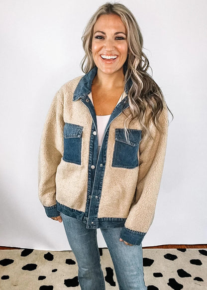 XL - A woman smiling wearing a heavyweight mixed-media jacket featuring a blue denim collar, placket, and chest pockets contrasted with a plush, beige sherpa body and sleeves.