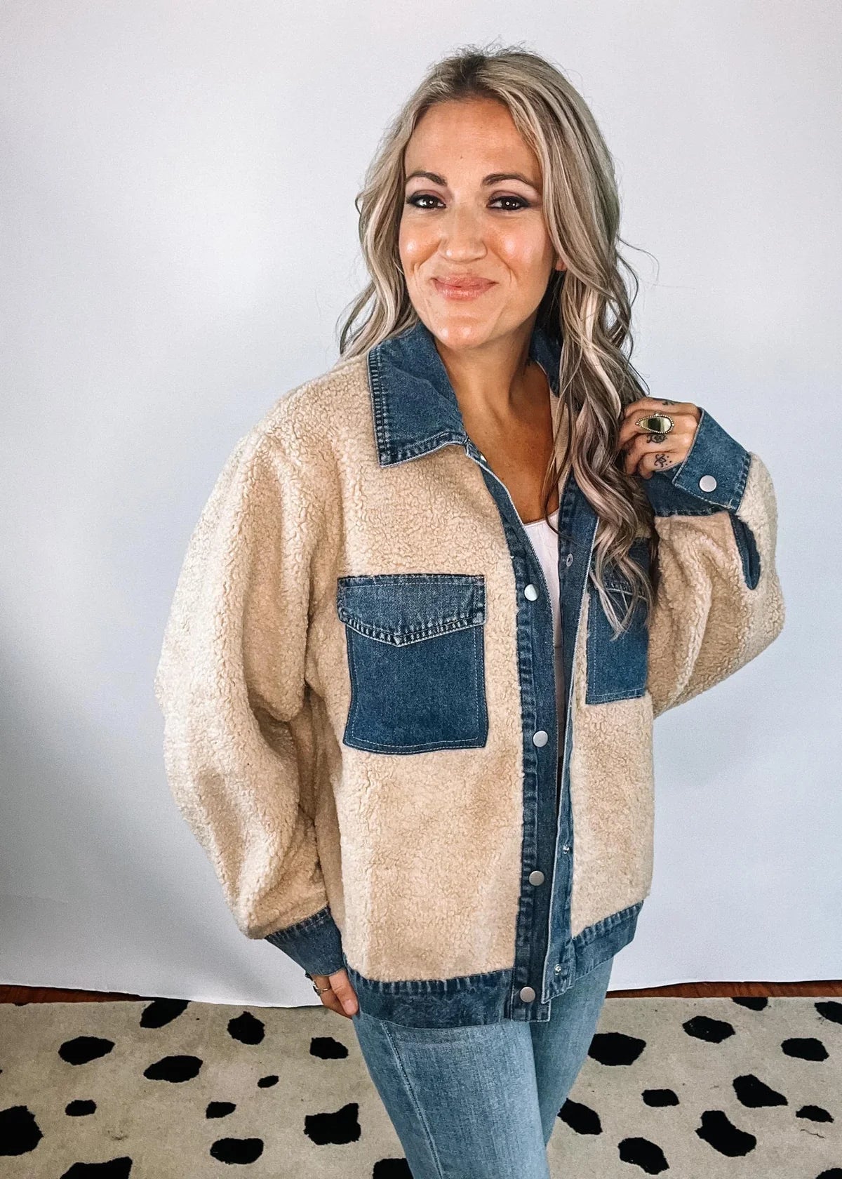 XL - A woman smiling wearing a heavyweight mixed-media jacket featuring a blue denim collar, placket, and chest pockets contrasted with a plush, beige sherpa body and sleeves.