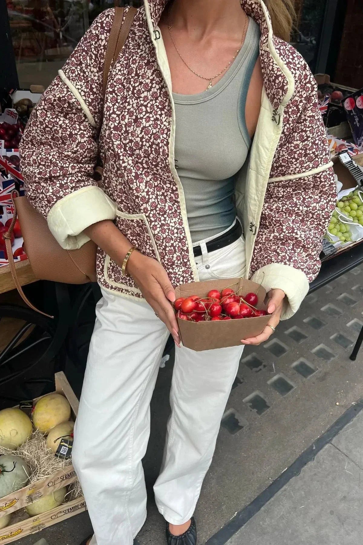 A woman wearing a quilted, floral print jacket with contrast piping and rolled cuffs over a ribbed tank top and white trousers.