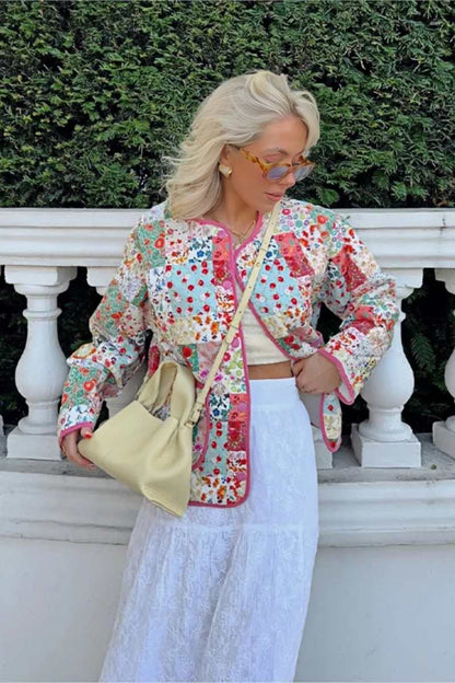 A woman wearing a vibrant, multi-floral patchwork quilted jacket with a collarless neckline and contrast piping, paired with a white skirt.