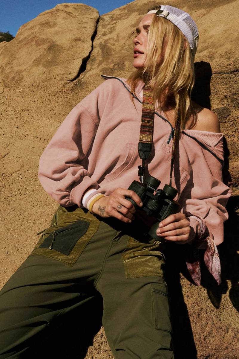 A woman wearing a dusty pink oversized half-zip sweatshirt with a high funnel neck, kangaroo pocket, and ribbed cuffs, paired with distressed denim shorts.