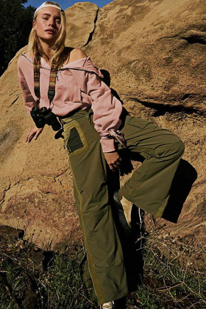 A woman wearing a dusty pink oversized half-zip sweatshirt with a high funnel neck, kangaroo pocket, and ribbed cuffs, paired with distressed denim shorts.