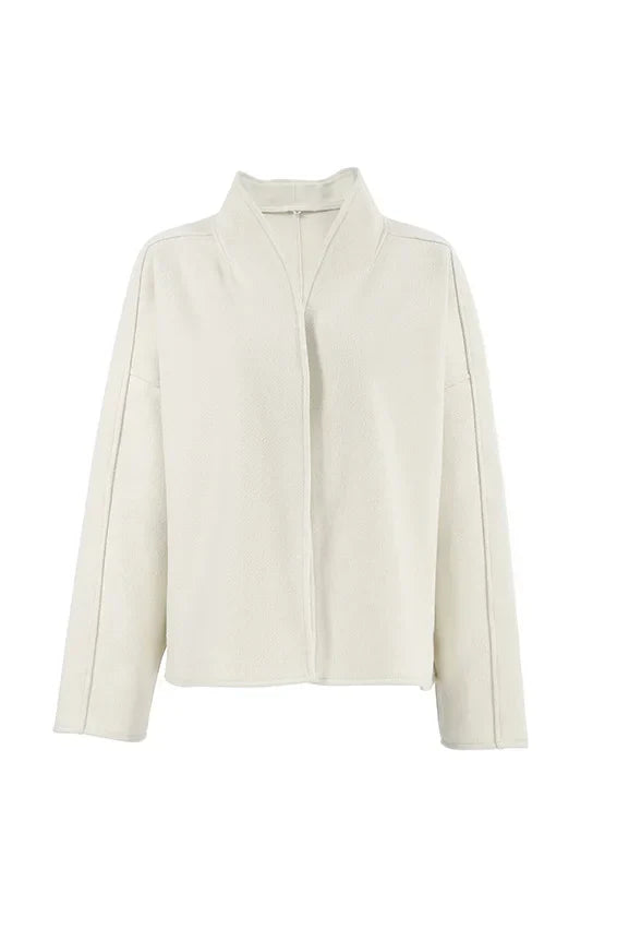 Apricot - Woman wearing an oversized, collarless, open-front cropped jacket in a light cream colour, styled over a white knit sweater and cream jeans.