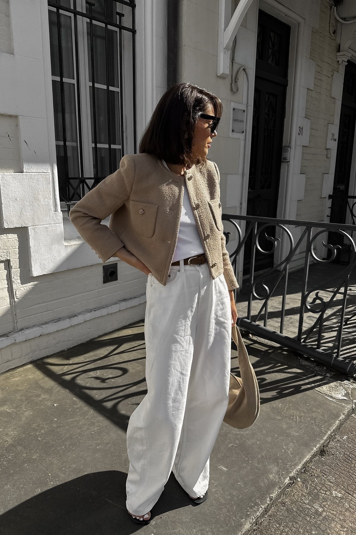 Women's smart casual textured cropped jacket in a neutral tone, featuring ornate buttons and a collarless design, styled over a white t-shirt and denim shorts.