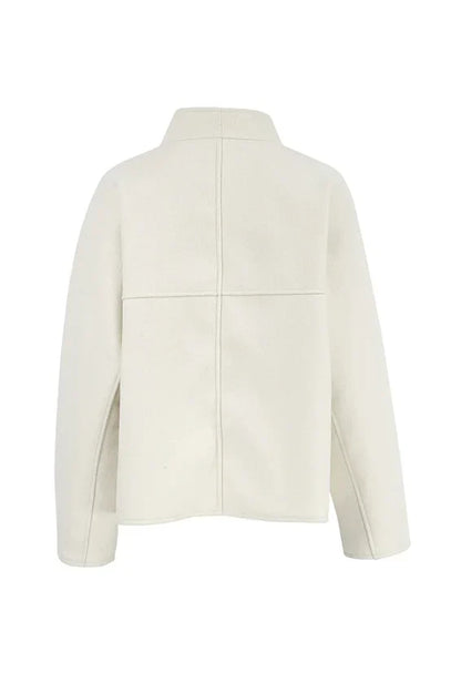 Apricot - Woman wearing an oversized, collarless, open-front cropped jacket in a light cream colour, styled over a white knit sweater and cream jeans.