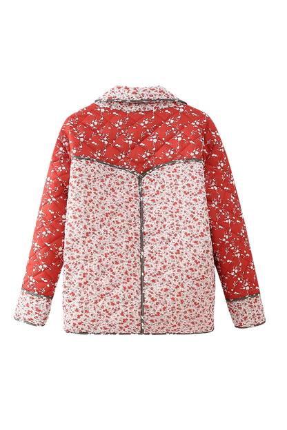 A woman wearing a hip-length quilted jacket featuring a mixed red and white floral print, contrast dark piping, and a button-front closure.
