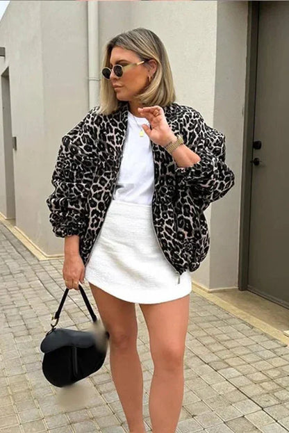 Leopard Print - A woman wearing an oversized bomber jacket with a leopard print, styled over a black crop top and beige ribbed mini skirt.