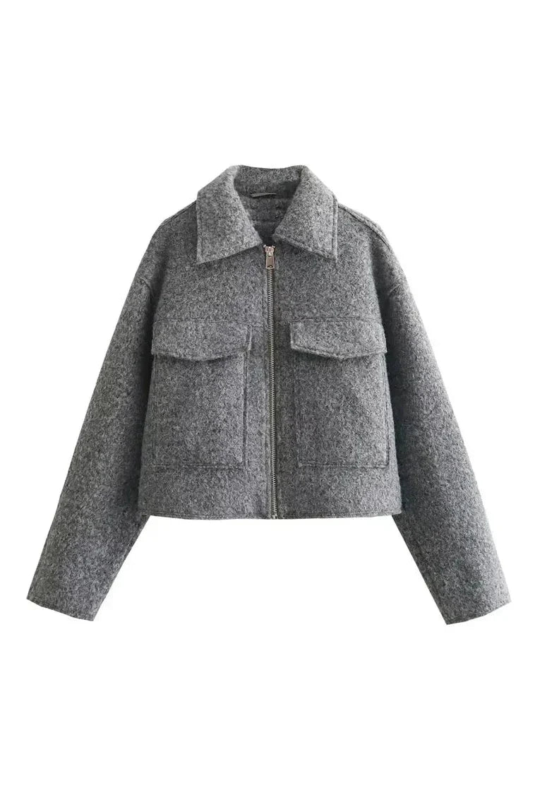 Gray - A woman wearing a women's grey textured cropped jacket with a silver front zipper and chest flap pockets, styled over a white t-shirt and black pleated mini skirt.