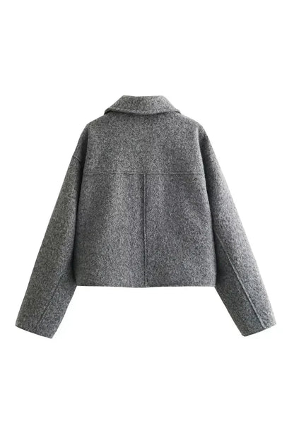 Gray - A woman wearing a women's grey textured cropped jacket with a silver front zipper and chest flap pockets, styled over a white t-shirt and black pleated mini skirt.