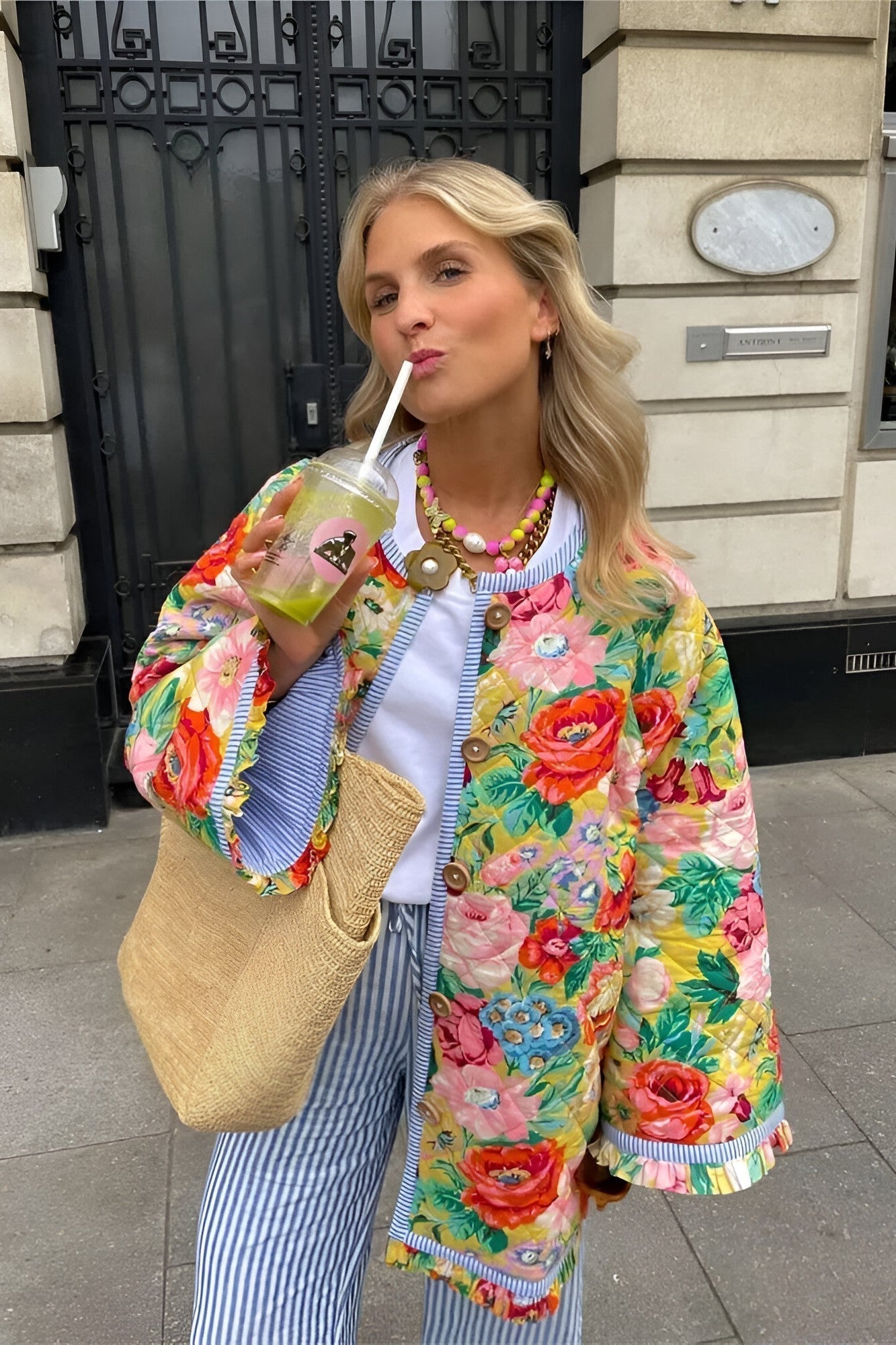 Women's longline quilted jacket featuring a bright, oversized floral print on a yellow background, finished with contrasting blue and white striped trim around the edges and cuffs, and a wooden-style button-front closure.
