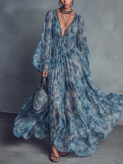 Blue - A model wearing a floor-length, long-sleeved maxi dress in a blue and grey abstract print chiffon, featuring a deep plunging V-neckline and voluminous balloon sleeves.