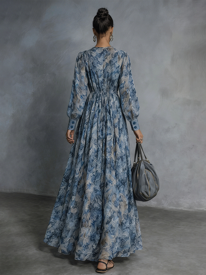 Blue - A model wearing a floor-length, long-sleeved maxi dress in a blue and grey abstract print chiffon, featuring a deep plunging V-neckline and voluminous balloon sleeves.