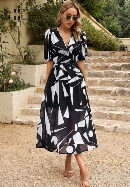 Black - Women's flowing midi dress featuring a V-neckline, half puff sleeves, and a large-scale abstract floral print in muted earthy tones, styled with a woven clutch.