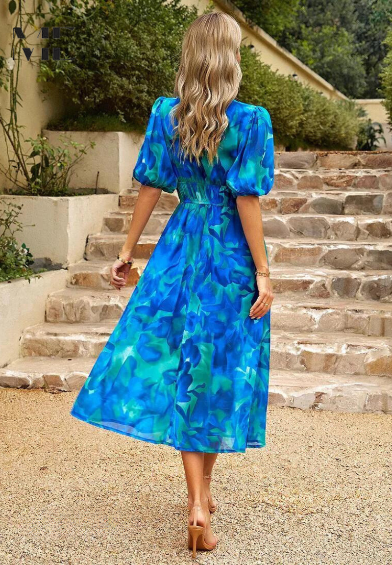 Floral - Women's flowing midi dress featuring a V-neckline, half puff sleeves, and a large-scale abstract floral print in muted earthy tones, styled with a woven clutch.