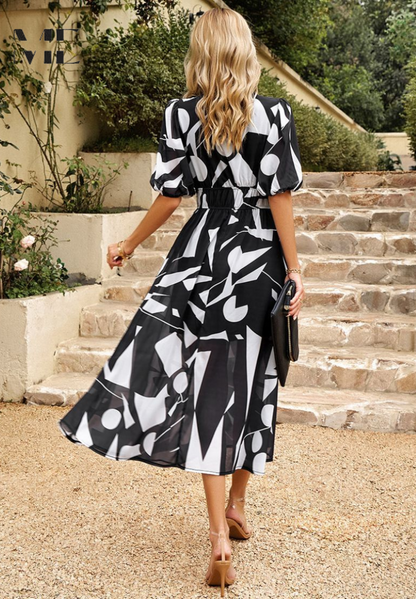Blue - Women's flowing midi dress featuring a V-neckline, half puff sleeves, and a large-scale abstract floral print in muted earthy tones, styled with a woven clutch.