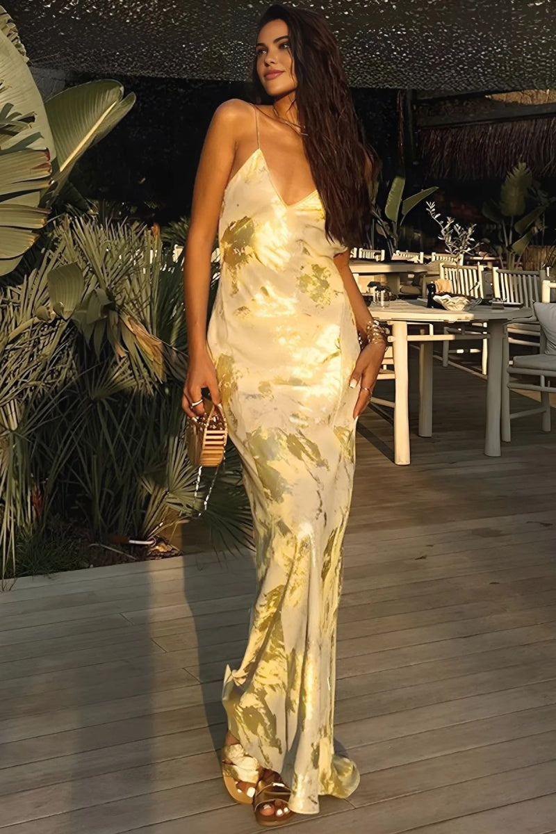 A woman wearing a sleeveless, floor-length satin slip dress with a gold and cream abstract print, featuring a V-neckline and thin straps.