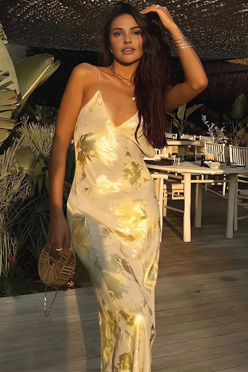 Gold - A woman wearing a sleeveless, floor-length satin slip dress with a gold and cream abstract print, featuring a V-neckline and thin straps.