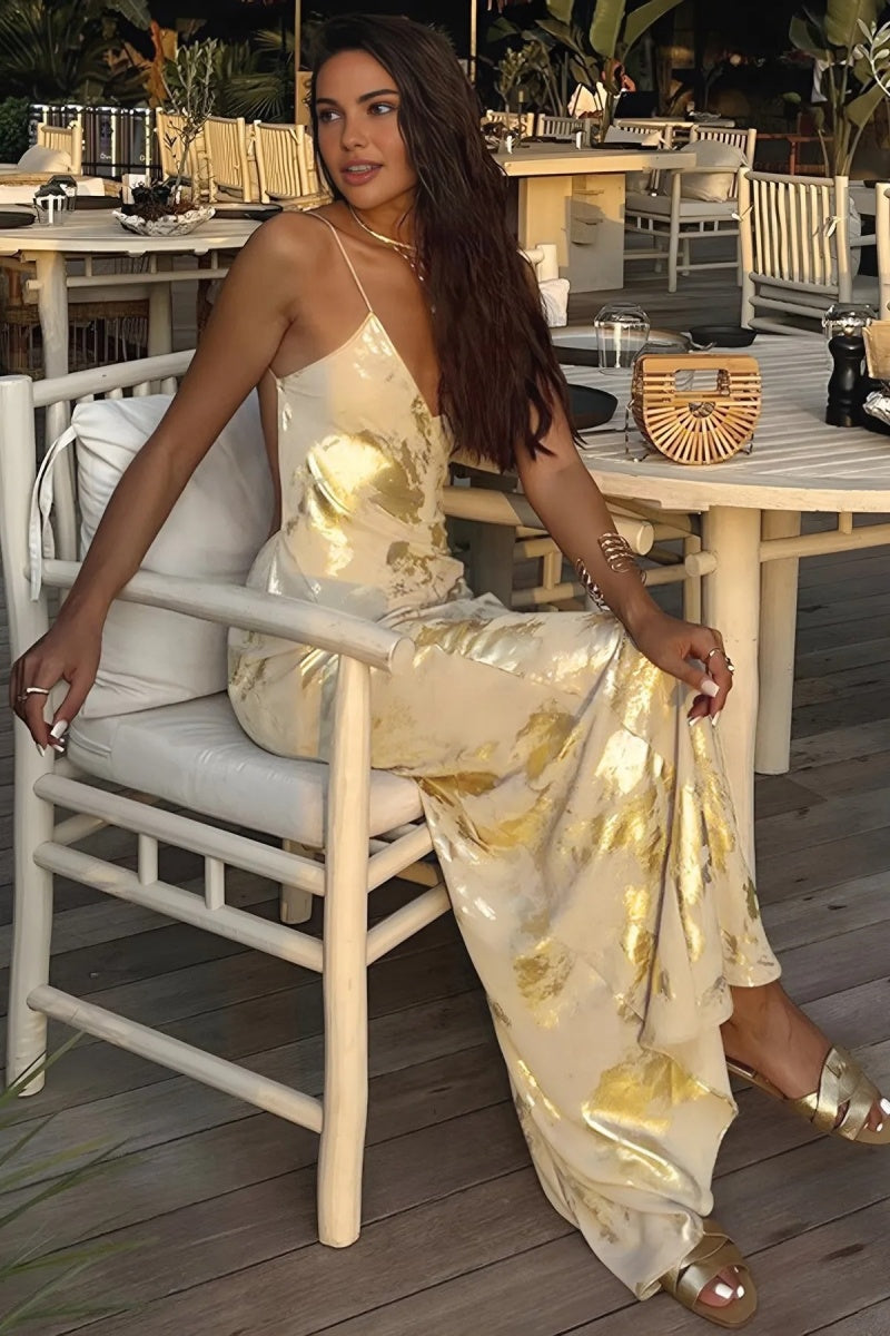 Gold - A woman wearing a sleeveless, floor-length satin slip dress with a gold and cream abstract print, featuring a V-neckline and thin straps.