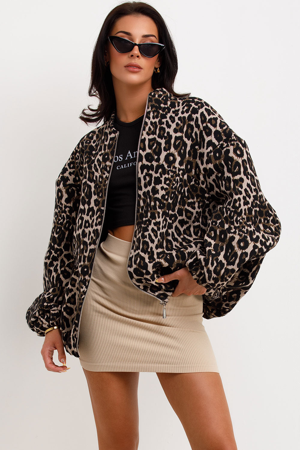 Leopard Print - A woman wearing an oversized bomber jacket with a leopard print, styled over a black crop top and beige ribbed mini skirt.