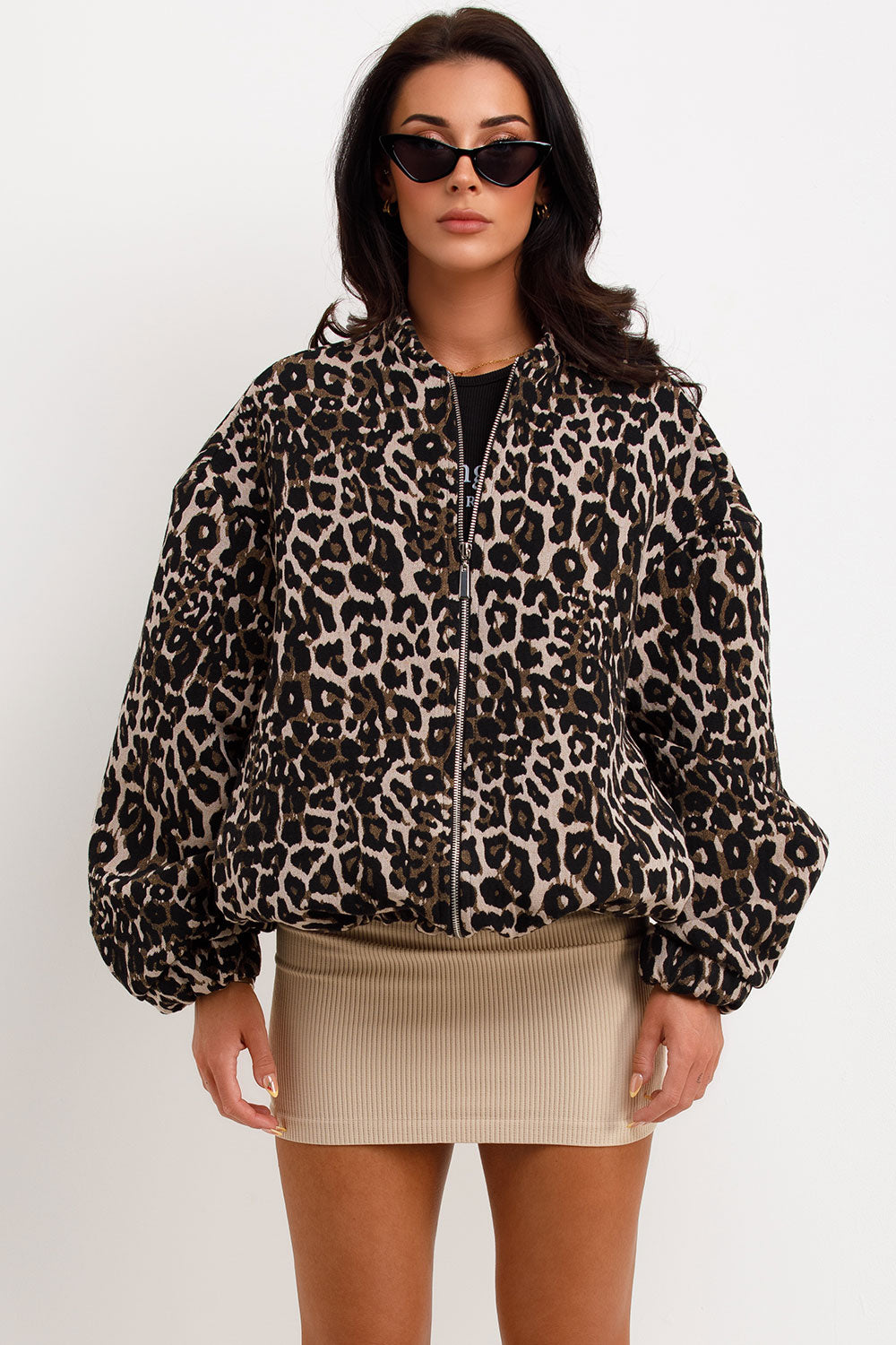 Leopard Print - A woman wearing an oversized bomber jacket with a leopard print, styled over a black crop top and beige ribbed mini skirt.