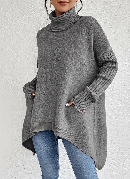 Gray - A woman wearing a blue oversized knit turtleneck sweater with ribbed sleeves and an asymmetrical high-low hem, paired with blue jeans.