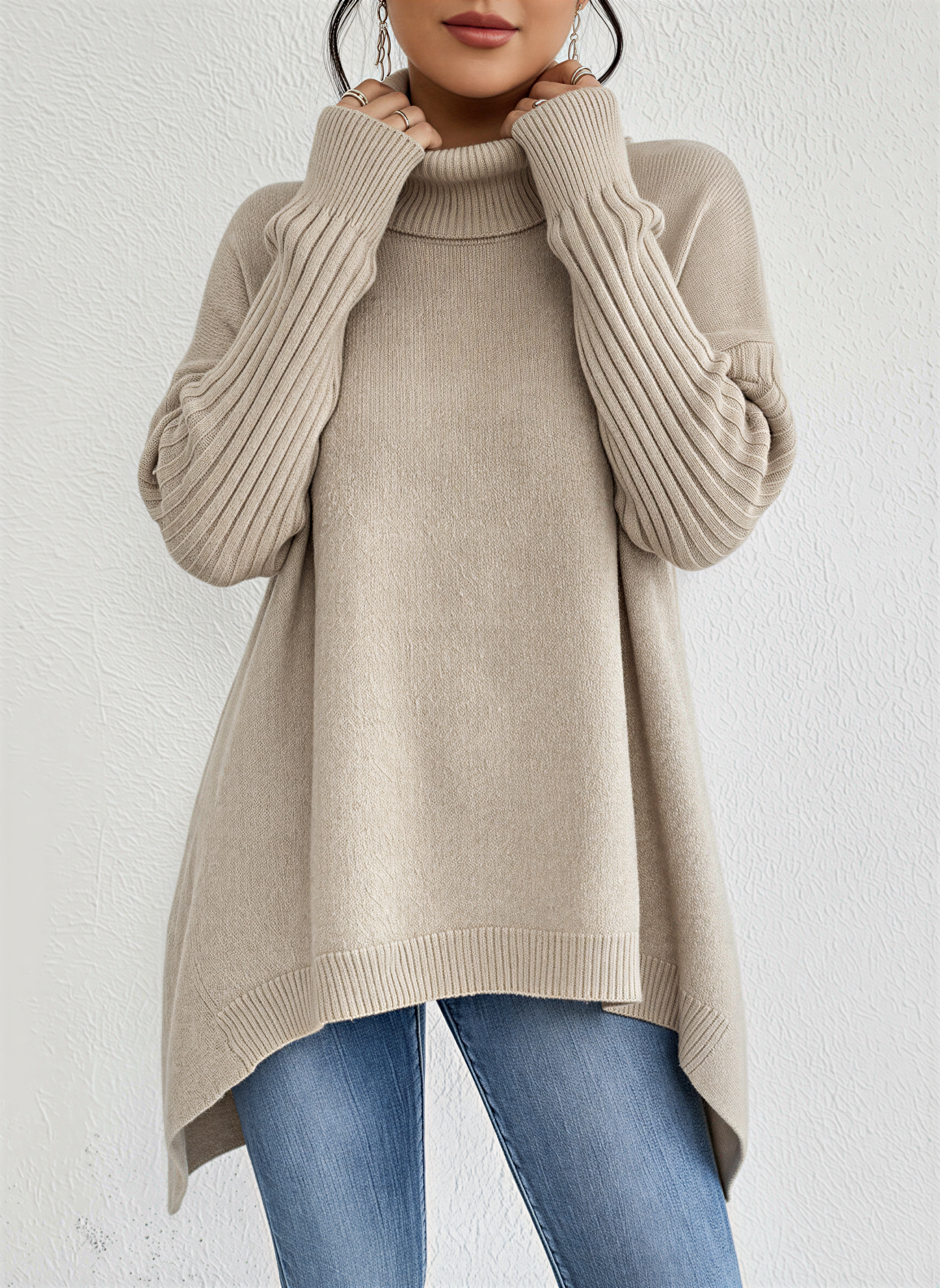 Beige - A woman wearing a blue oversized knit turtleneck sweater with ribbed sleeves and an asymmetrical high-low hem, paired with blue jeans.