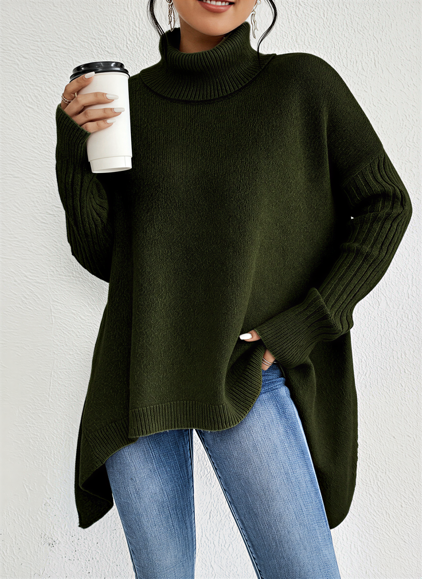 Green - A woman wearing a blue oversized knit turtleneck sweater with ribbed sleeves and an asymmetrical high-low hem, paired with blue jeans.
