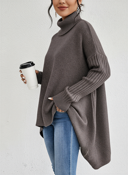 Brown - A woman wearing a blue oversized knit turtleneck sweater with ribbed sleeves and an asymmetrical high-low hem, paired with blue jeans.