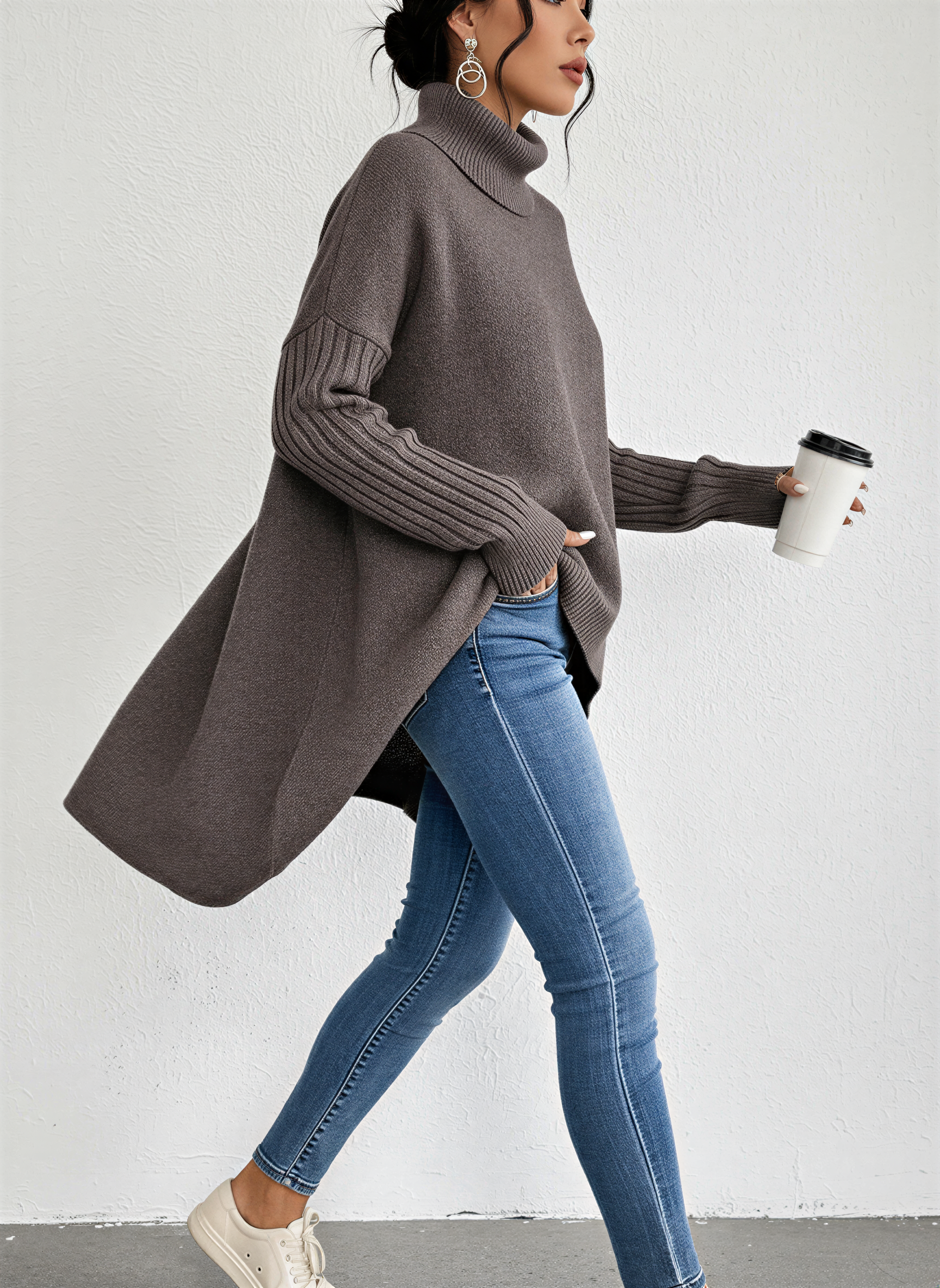 Brown - A woman wearing a blue oversized knit turtleneck sweater with ribbed sleeves and an asymmetrical high-low hem, paired with blue jeans.