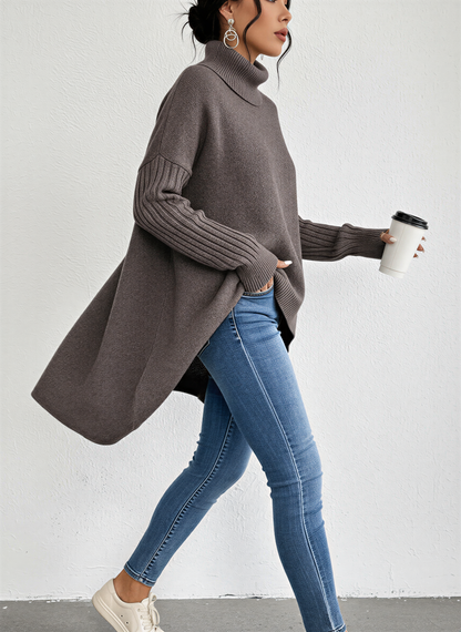 Brown - A woman wearing a blue oversized knit turtleneck sweater with ribbed sleeves and an asymmetrical high-low hem, paired with blue jeans.